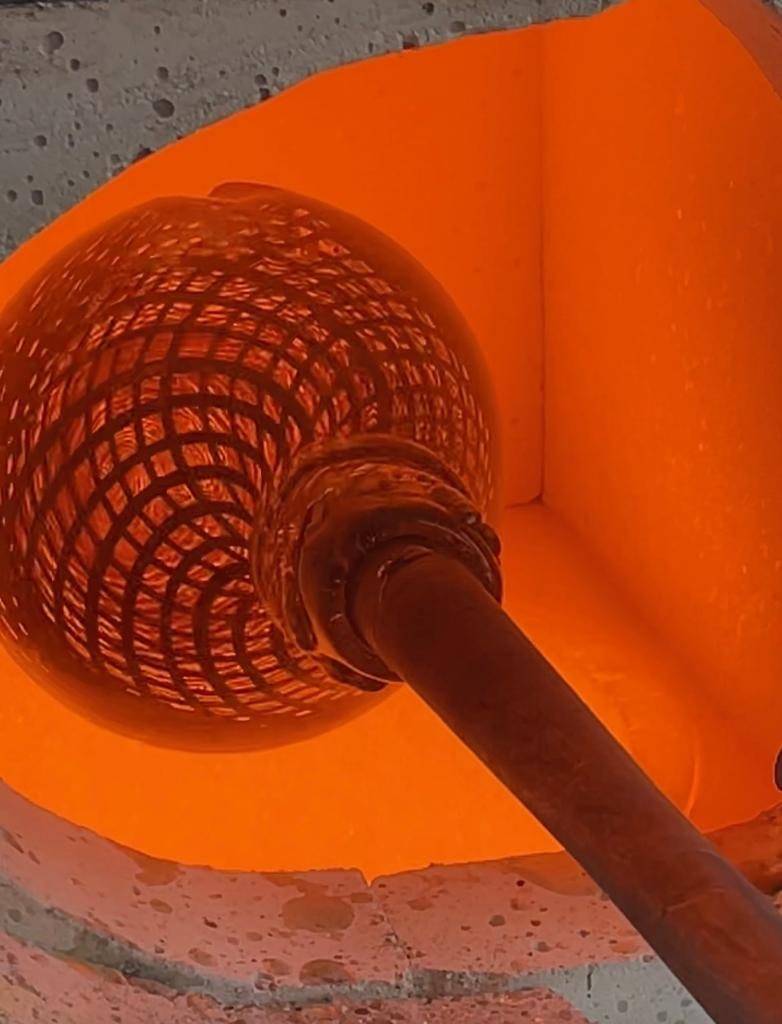 Glowing hot reticello glass sphere on blowpipe in the furnace showing the cane grid pattern